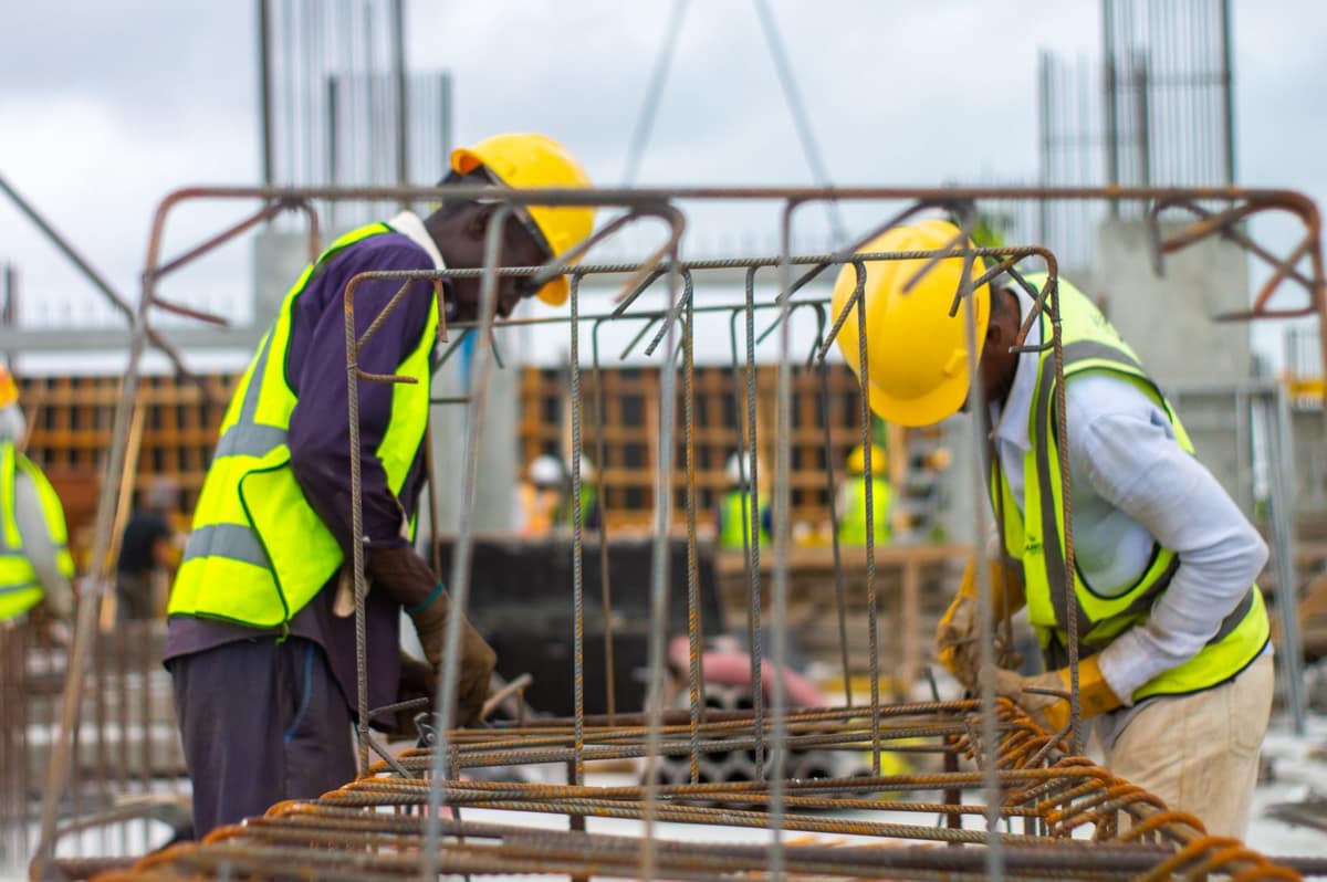 Two crew members in hard hats and safety vests tying rebar on a concrete deck